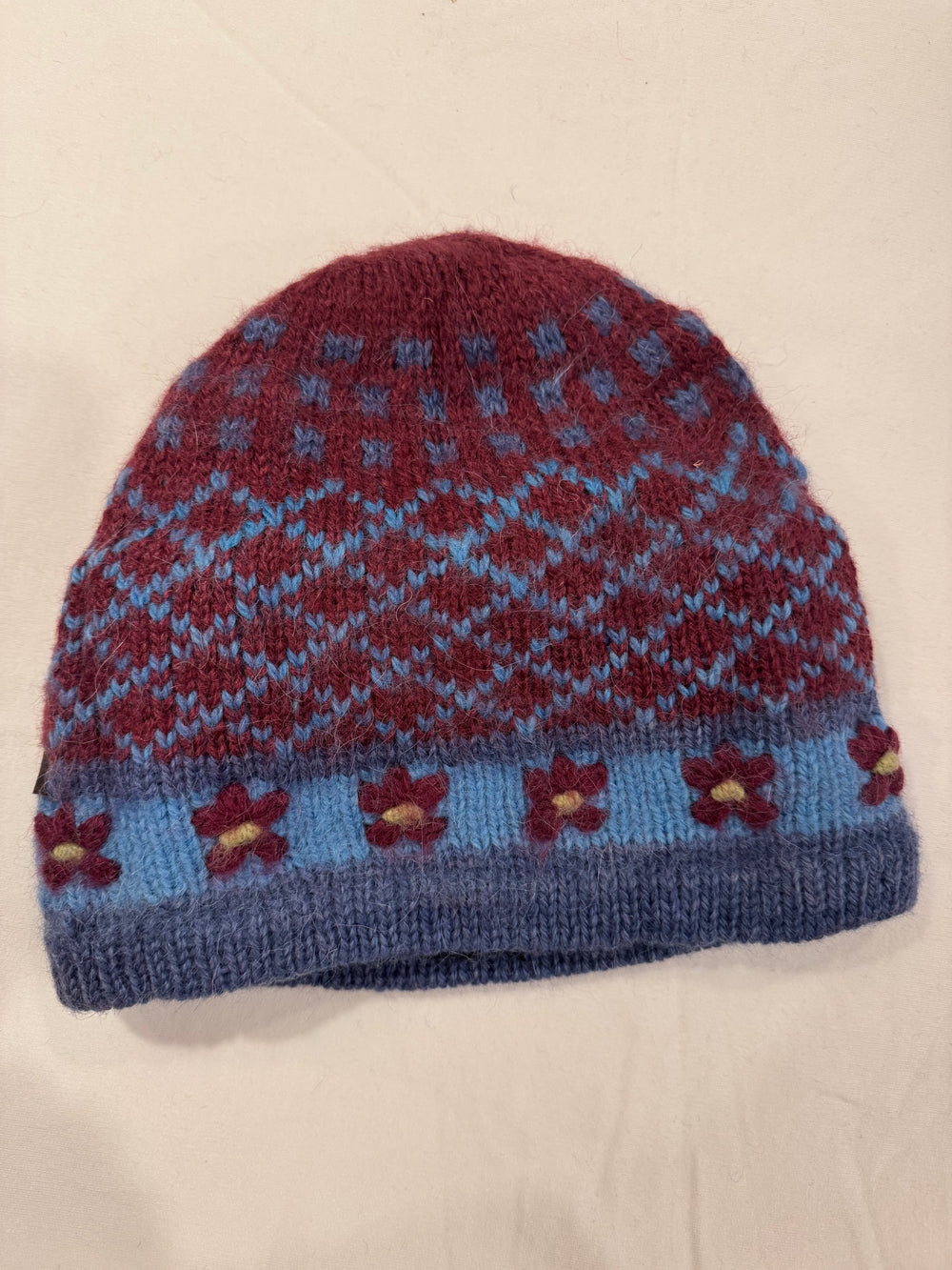 Burgundy Blooms alpaca beanie with a blue Fair Isle diamond pattern and hand-embroidered burgundy flowers with yellow centres on a pale blue band