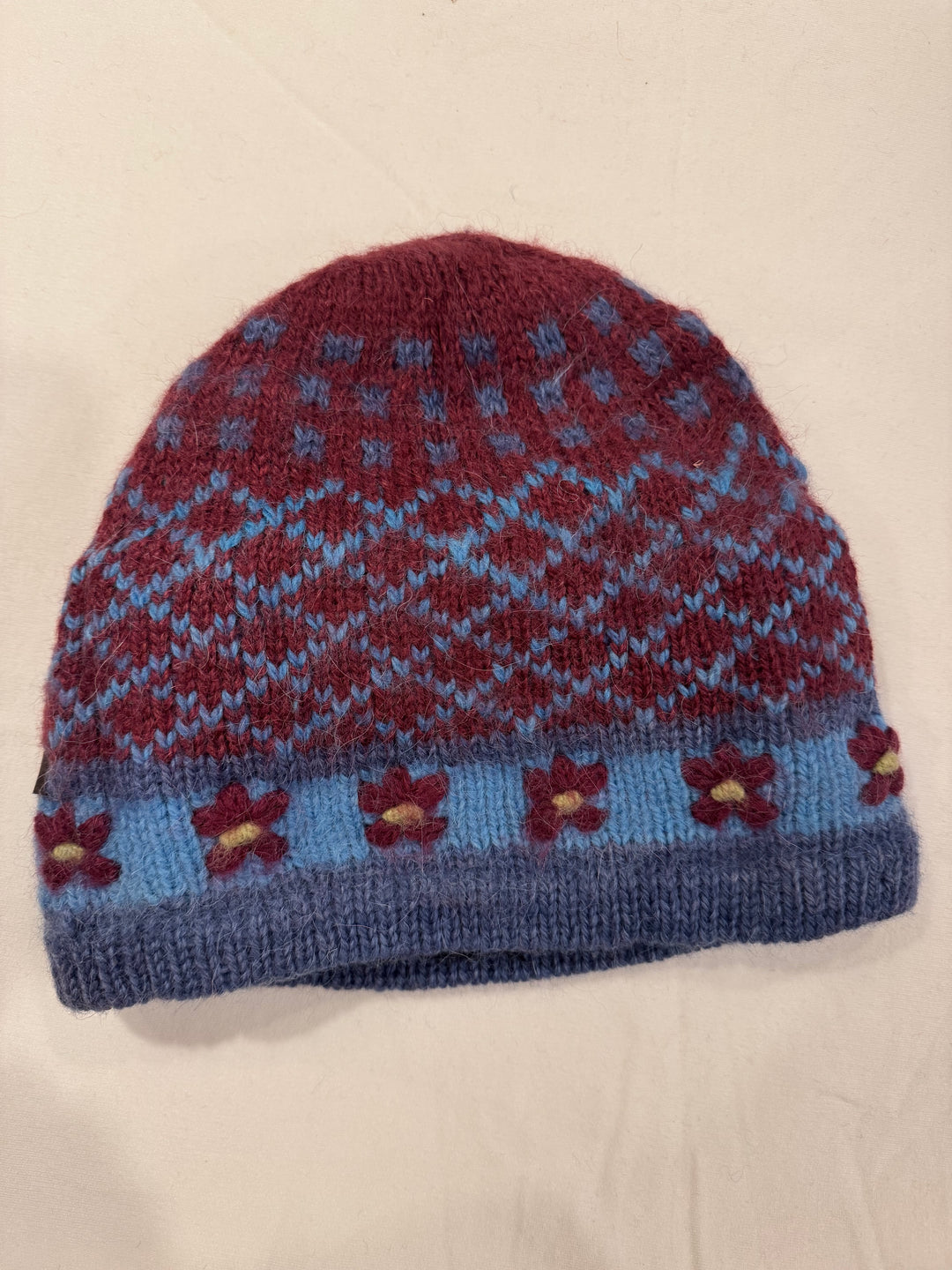 Burgundy Blooms alpaca beanie with a blue Fair Isle diamond pattern and hand-embroidered burgundy flowers with yellow centres on a pale blue band