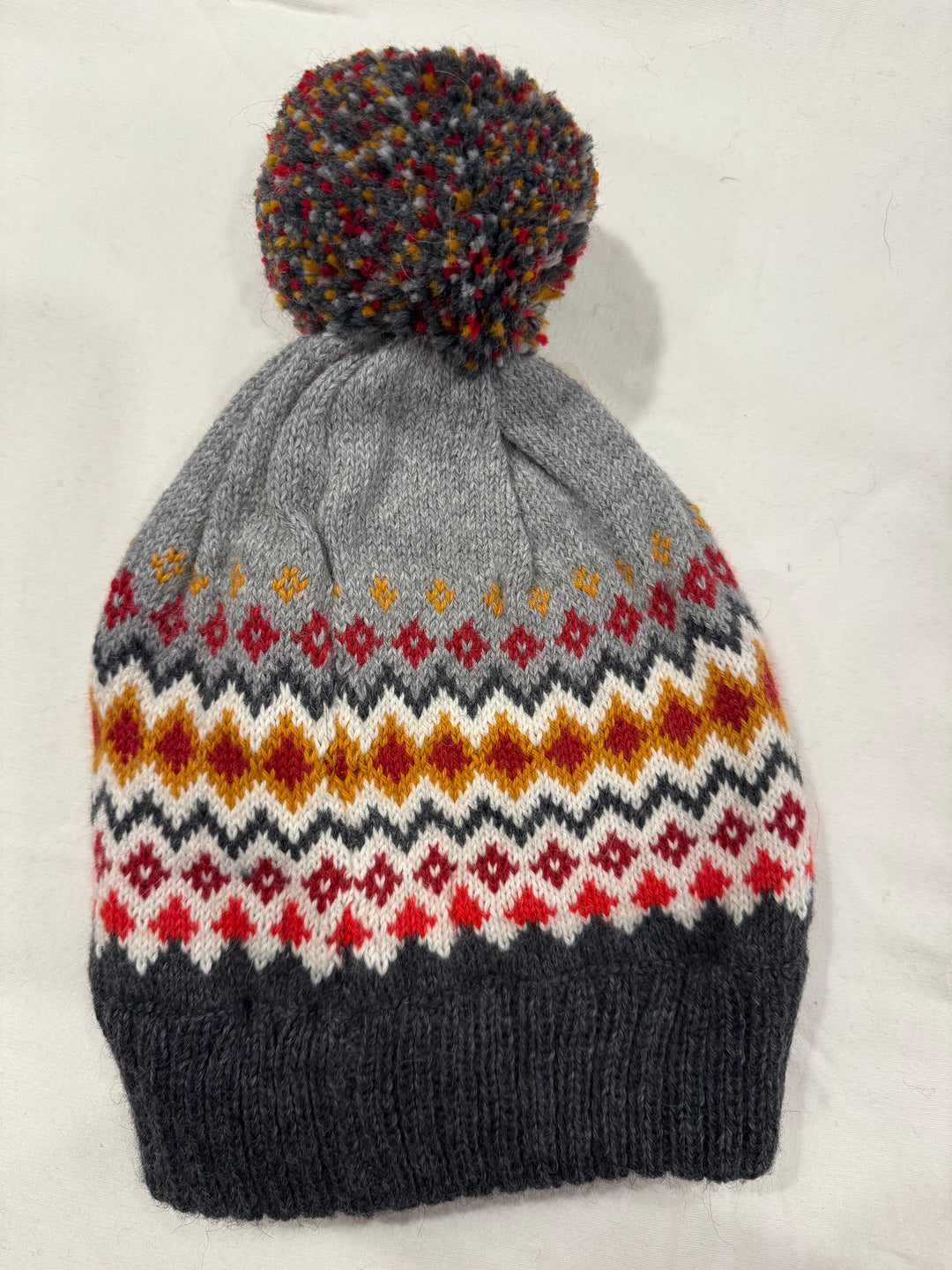 Fair Isle alpaca blend beanie in rust, gold and cream on a gray crown with a multicolor pom