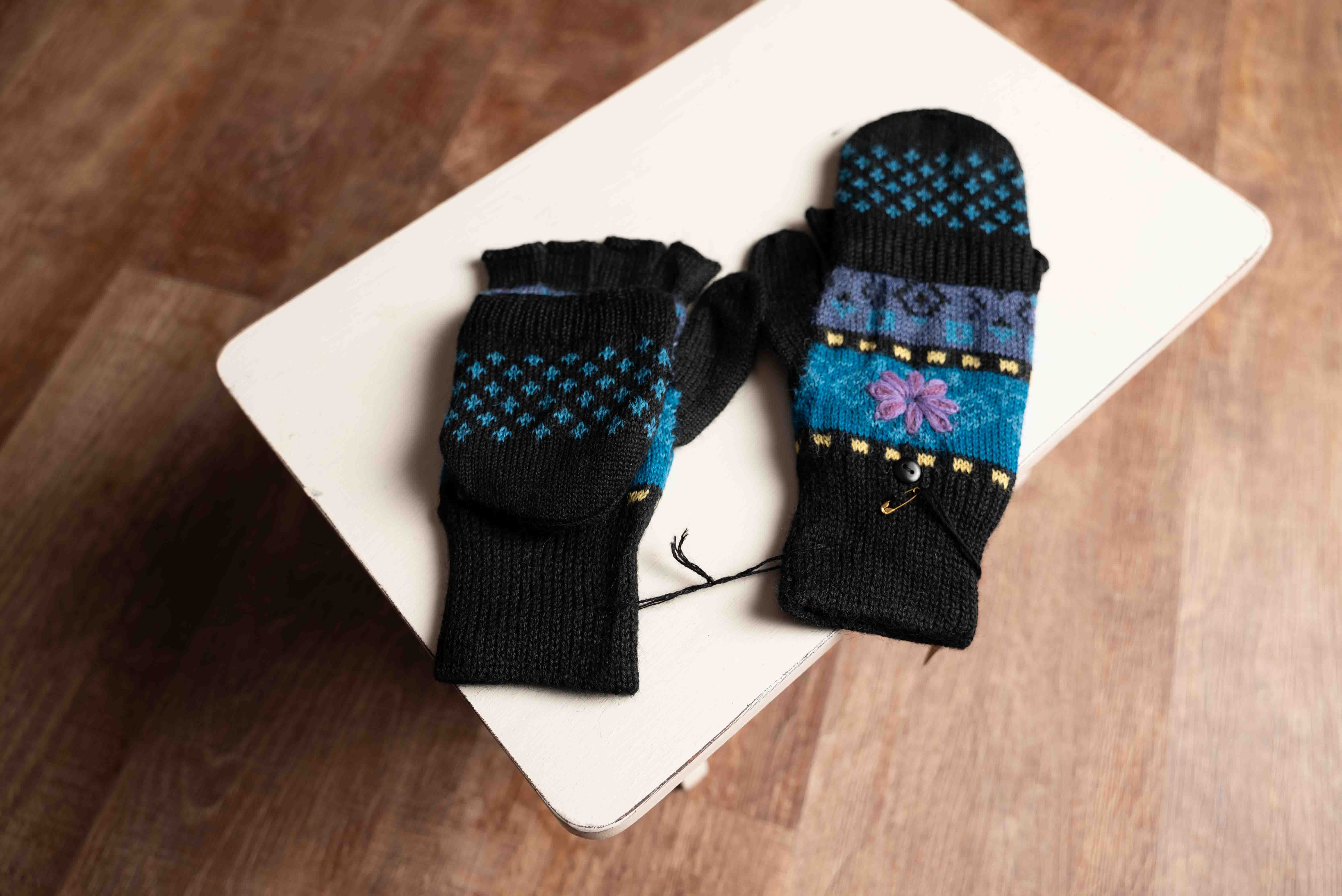A pair of blue alpaca lined glittens with a floral design, displayed on a wooden surface.