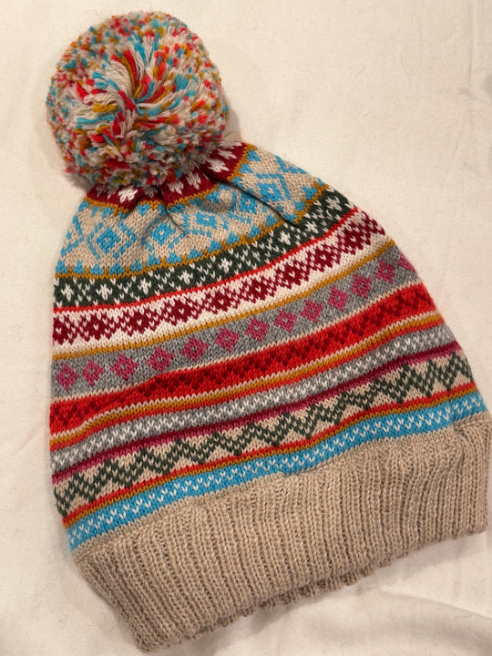 Alpine Confetti hand-knit beanie with narrow Fair Isle bands in turquoise, crimson, gold and sage on an oatmeal crown, topped with a multicolour flecked pom