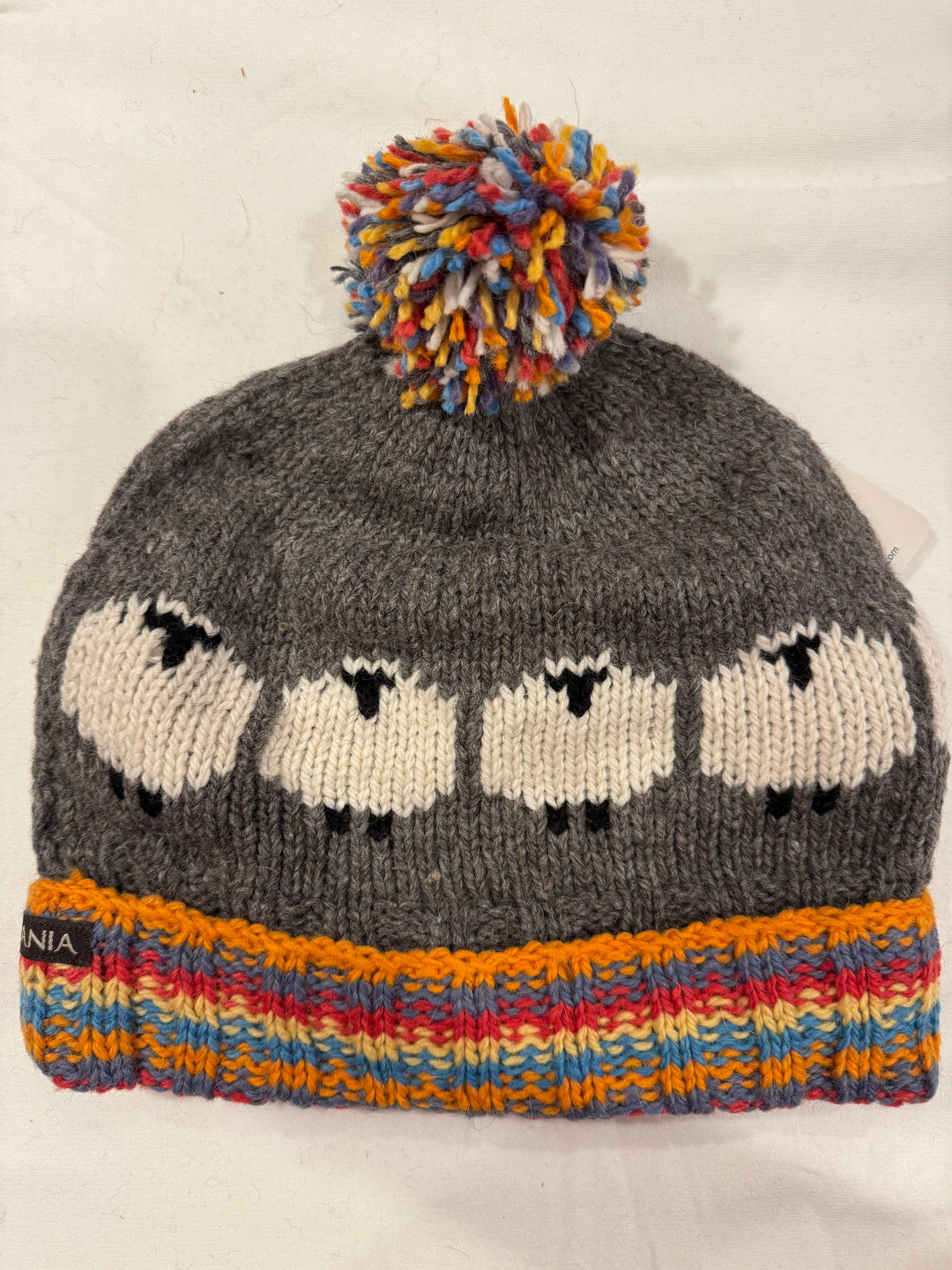 Beanie with knitted cream sheep on a gray crown and a rainbow striped cuff, 100% alpaca