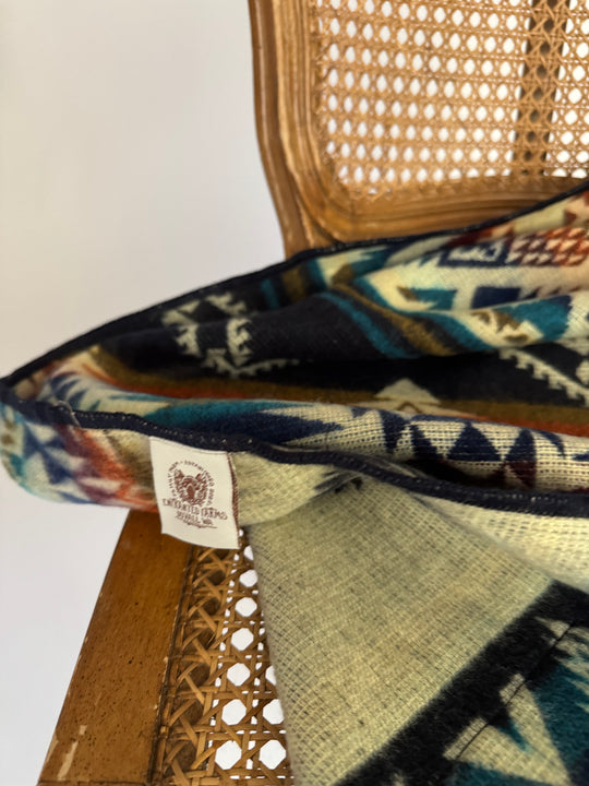 Close-up of a patterned fabric with a visible brand tag on a woven surface. Close-up of the Cuzco Plaza de Armas Alpaca Wool Blanket showing detailed stitching and soft woven texture.