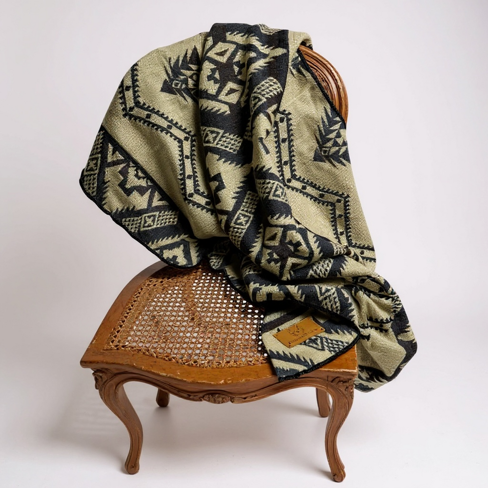 Cuzco Stone Alpaca Wool Blanket elegantly displayed on a light-wood vintage chair against a simple background.
