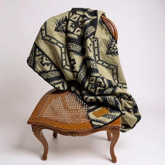 Cuzco Stone Alpaca Wool Blanket elegantly displayed on a light-wood vintage chair against a simple background.
