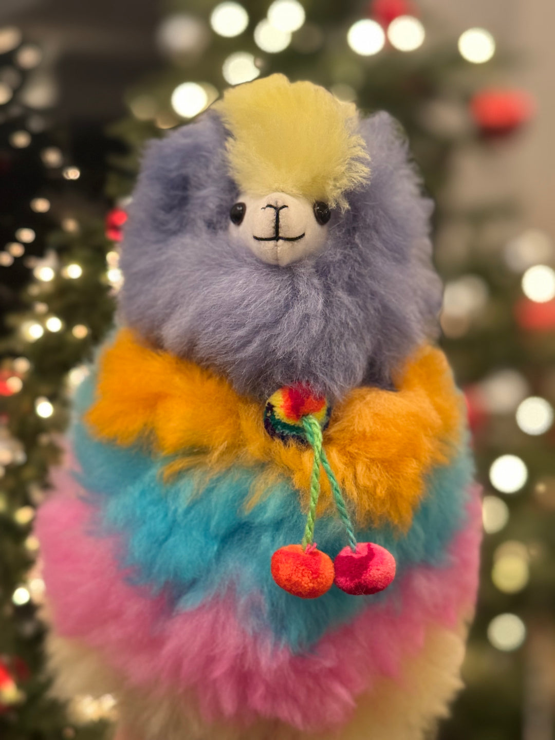 Multicolored plush llama toy with a blurred Christmas tree background