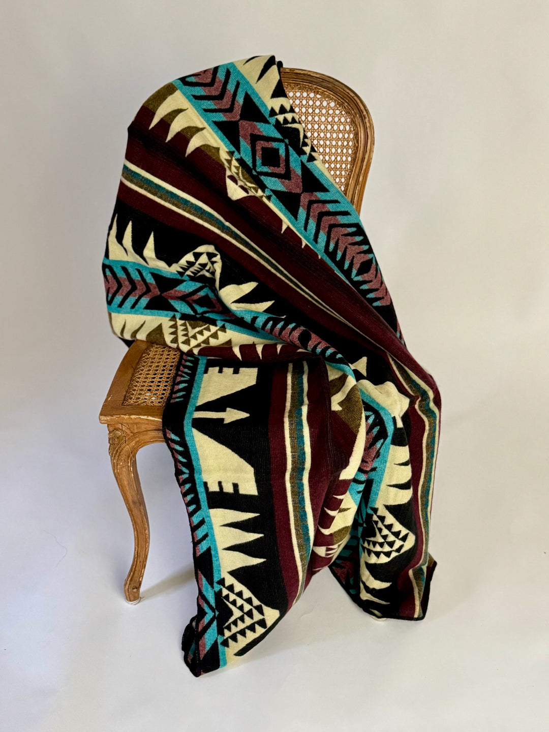 Patterned blanket draped over a wooden chair on a white background